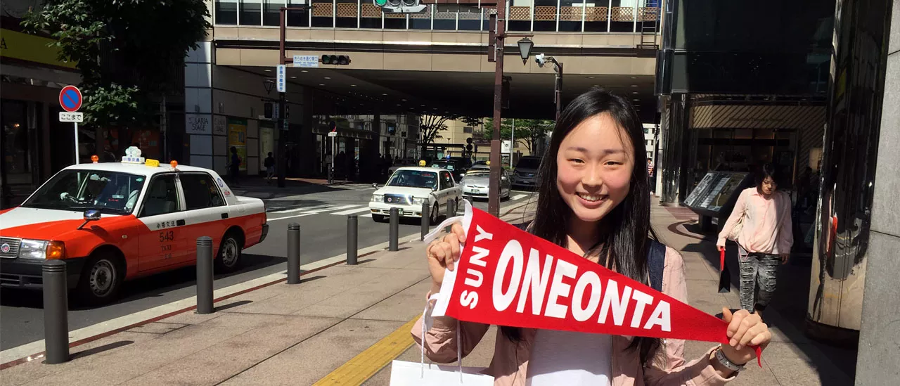 international student holding SUNY Oneonta banner