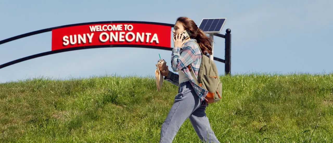 Student walking in front of the welcome to Suny Oneonta sign.