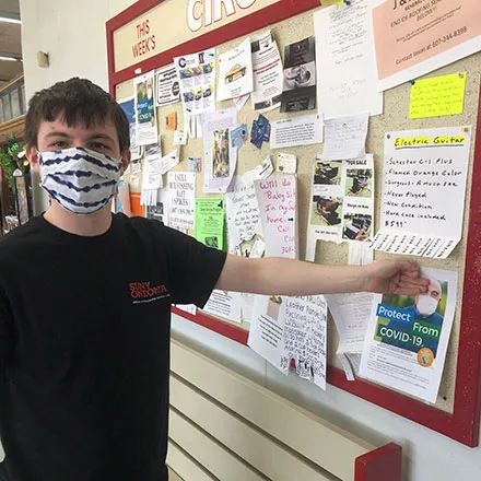Student in mask posting COVID vaccination flyer on bulletin board