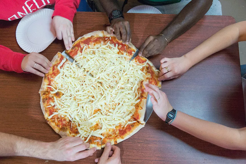 Students grabbing at slices of a pizza pie.