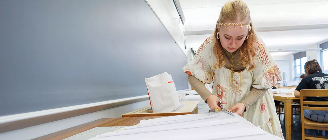 Fashion student cutting a piece of fabric with scissors.