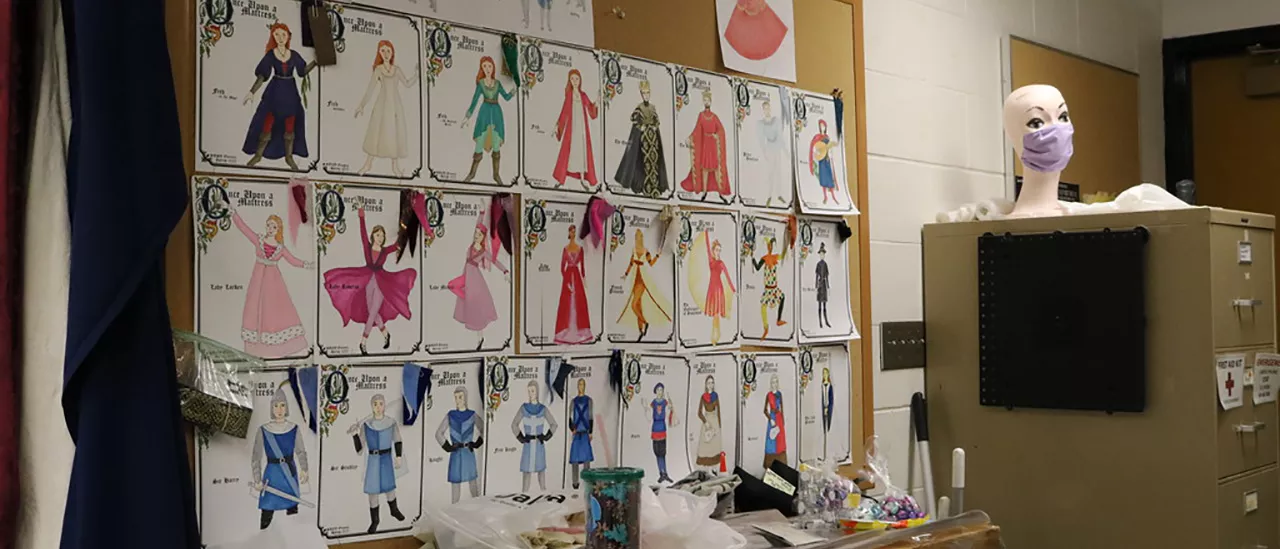 Photo featuring costume renderings from Once Upon a Mattress pinned to the cork board in the costume shop