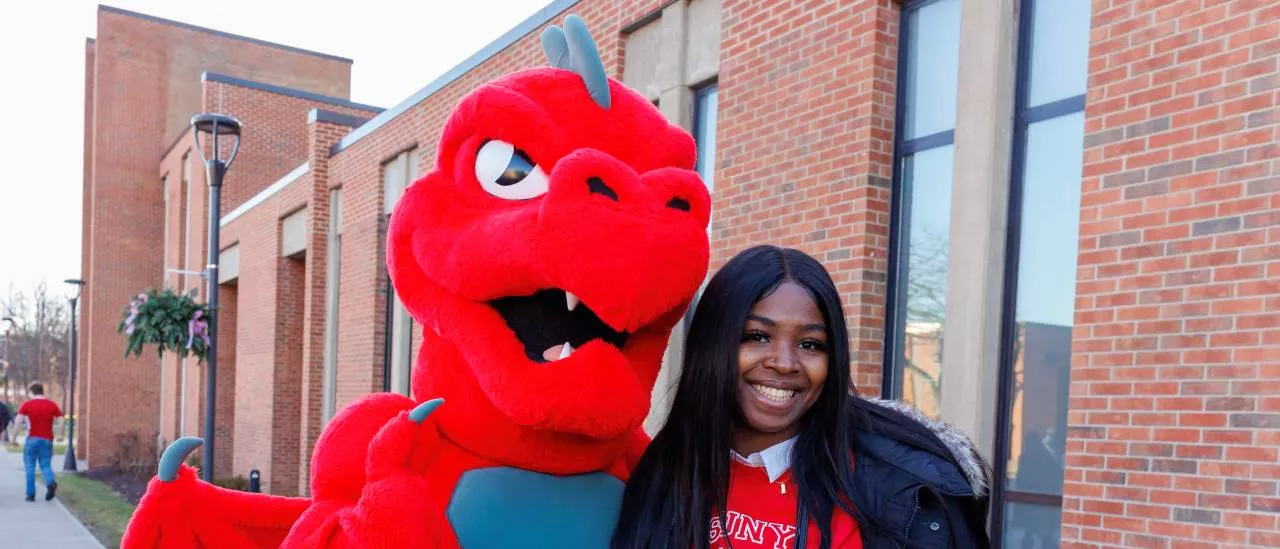 A student posing for a photo with Red the Dragon at Spring Pass Through the Pillars.