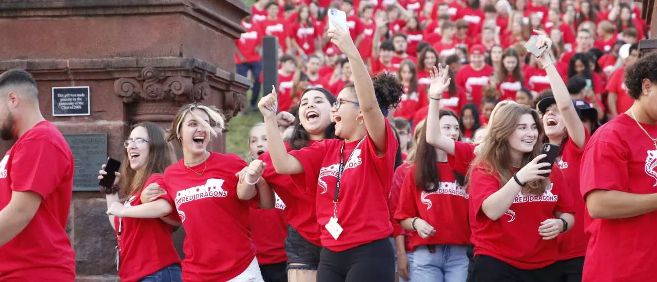 A large group of students moving through the pillars during Pass Through the Pillars and taking selfies.