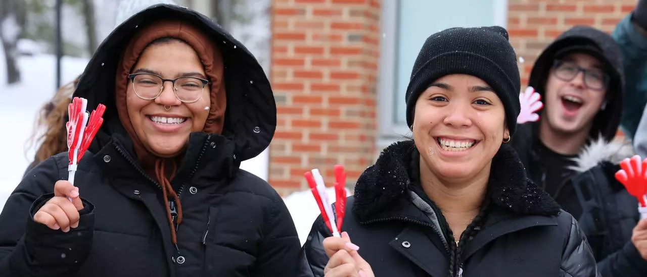Two students smiling while holding clappers at the Pass Through the Pillars event. 