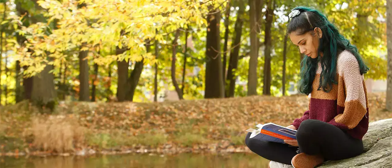 Person reading on a rock next to SUNY Oneonta's Hunt Union Pond