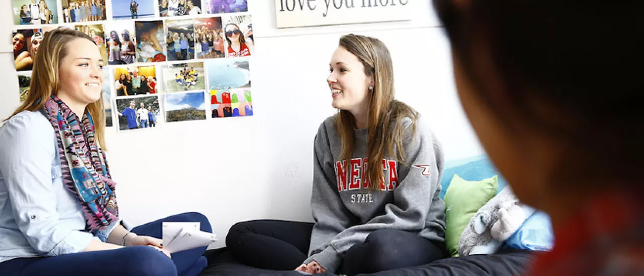 Female students talking on their bed in their dorm.