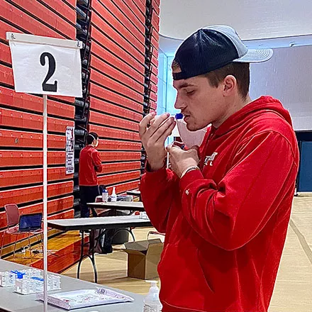 Student doing a COVID-19 saliva test at the Alumni Field House pool testing center