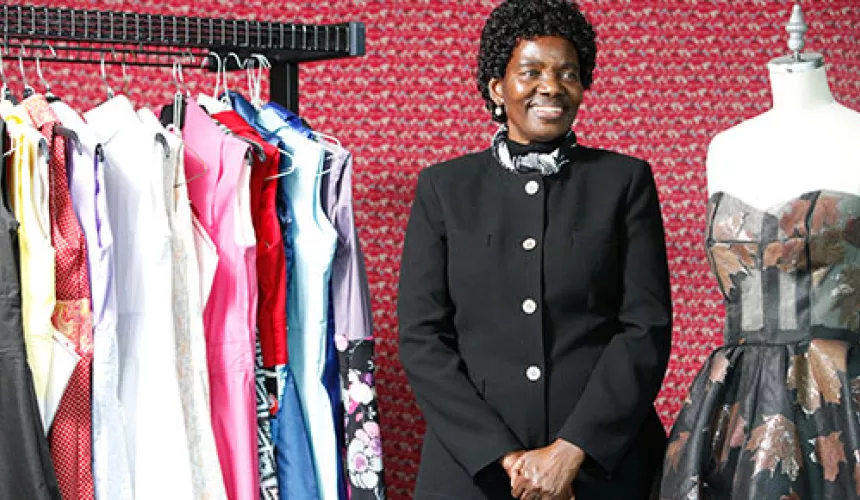Annacleta Chiweshe stands between a rack of dresses and a dress form
