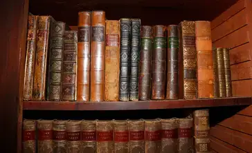 Old leather bound hard copy books sit on a shelf