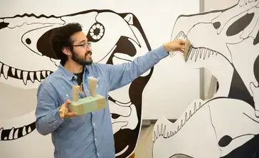 Museum Studies student holding 3 dinosaur teeth and showing the location of that tooth on a at-scale dinosaur cutout