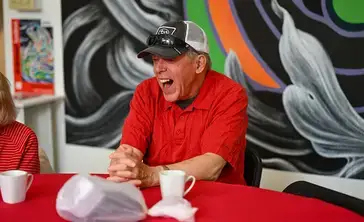 An alumnus in a red polo and baseball cap laughing.