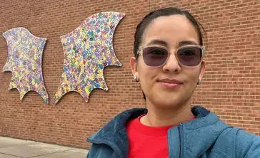 Emely Lopez posing in front of the dragon wings mural photo op on the Chase Physical Education building