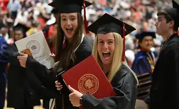 Undergraduates with wide smiles displaying their earned diplomas at graduation.