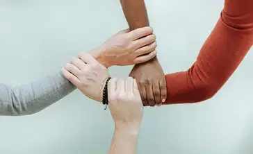 Multi-cultural hands grasping wrists in a show of connectedness.