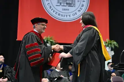 Recently hooded master's graduate receiving their diploma during Commencement