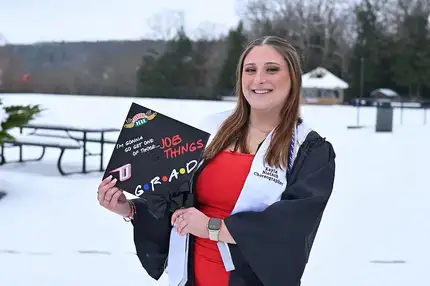 Graduate holding their decorated cap while standing on a snow covered ground