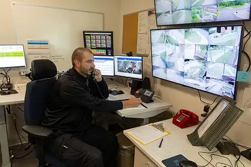 University Police dispatcher on the phone with large displays showing multiple camera views on the wall