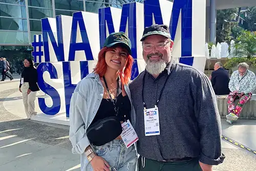Professor and student in from of 2026 NAMM sign