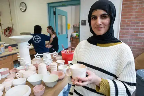 Student proudly displays their piece of pottery in the ceramics studio.