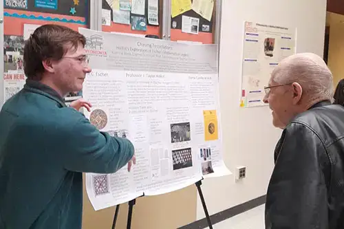 Daniel Schlagel explaining research poster to older man