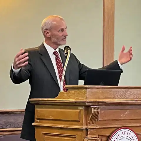 Dr. Jeffrey Wagner stands at a podium with arms stretched open while giving a talk.