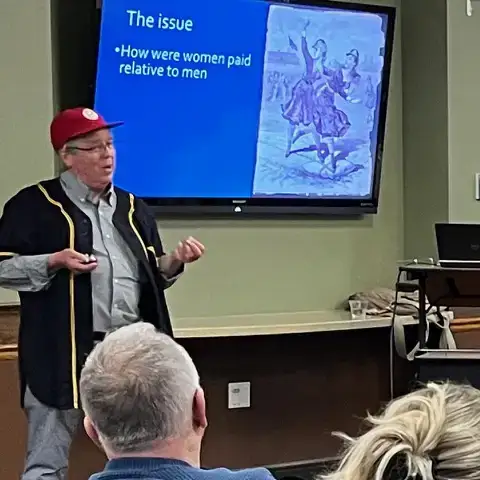 Dr. Michael Haupert, wearing a red baseball cap and dark baseball shirt, gives a talk.