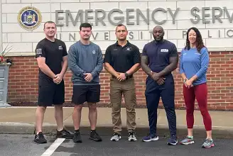 Diverse group of Physical Fitness instructors pose in front of the Emergency Services Building.