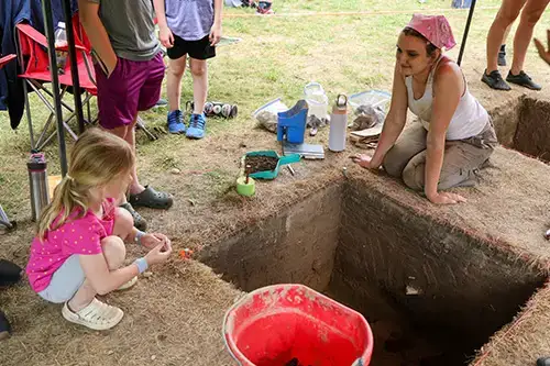 Archaeology student speaks with young girl at dig site