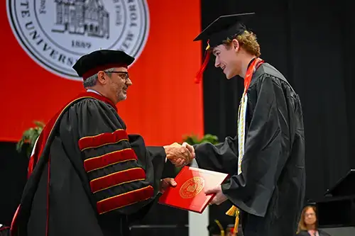 Alberto Cardelle at Commencement handing a student their diploma