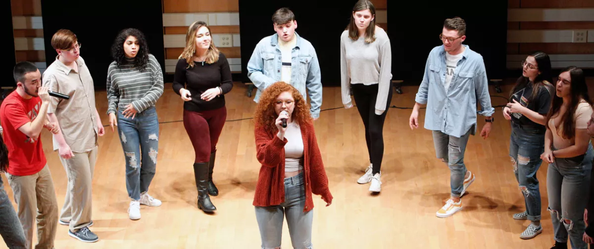 Girl singing with a group of students singing around her.