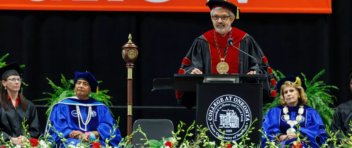 President Cardelle speaking at a podium while wearing academic regalia