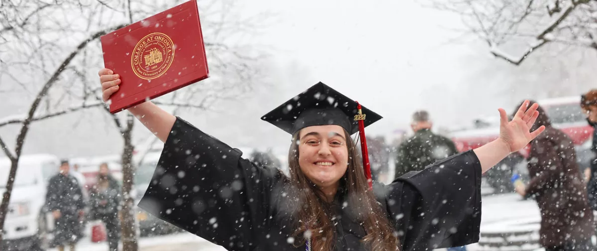 Student smiling holding her diploma during a snow storm.