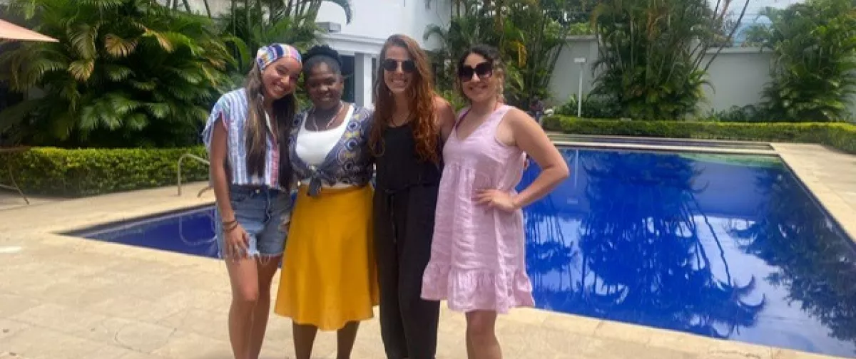 Four women smiling, standing in front of a pool.