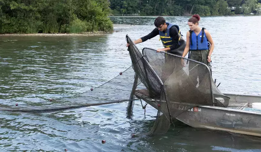 Two students collection samples shown pulling a net onto a boat on Otsego Lake.