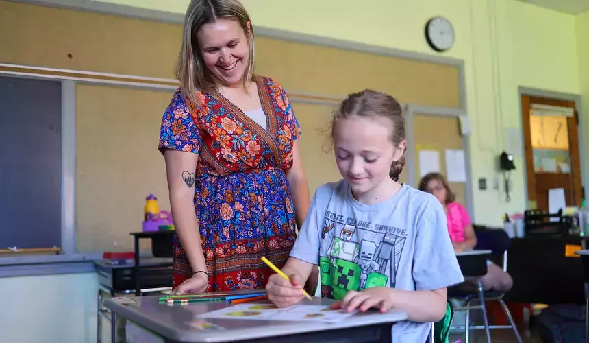M.S. Ed. student assists child during a writing assignment in the classroom.