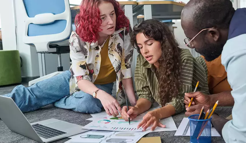 Two young women pointing at a document of charts during statistics discussion