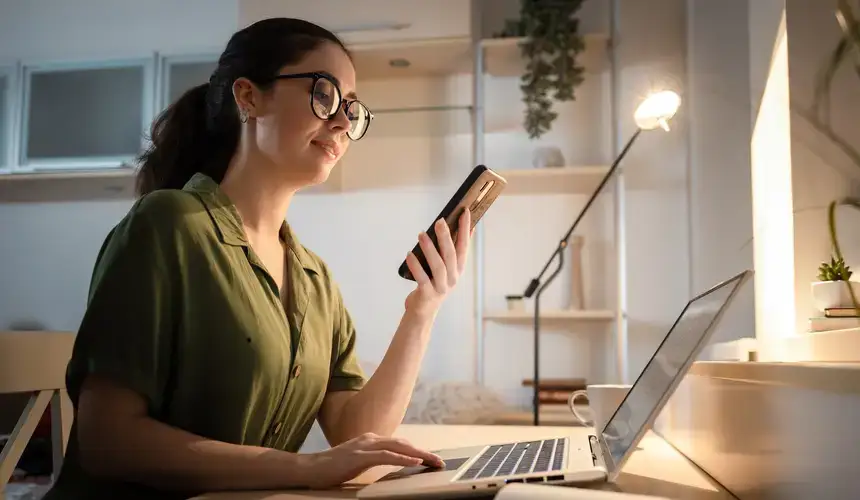 Caucasian smiling young person using cellphone and working at laptop.