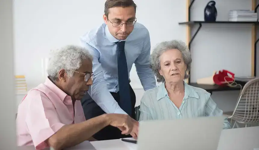 A man in a shirt and tie helps a diverse elderly couple with a computer.