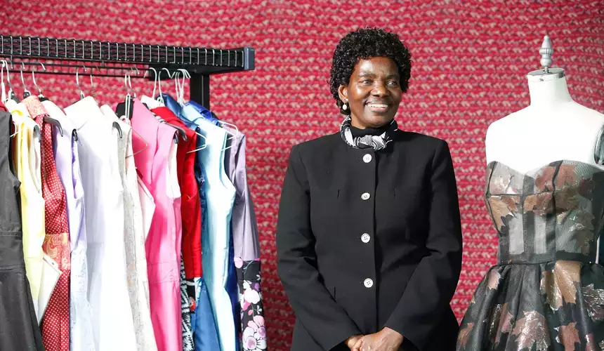Annacleta Chiweshe stands between a rack of dresses and a dress form