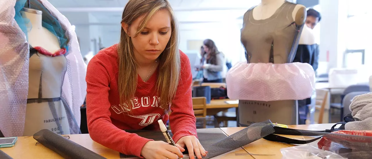 Fashion student marking fabric to be used on clothing being developed behind them.