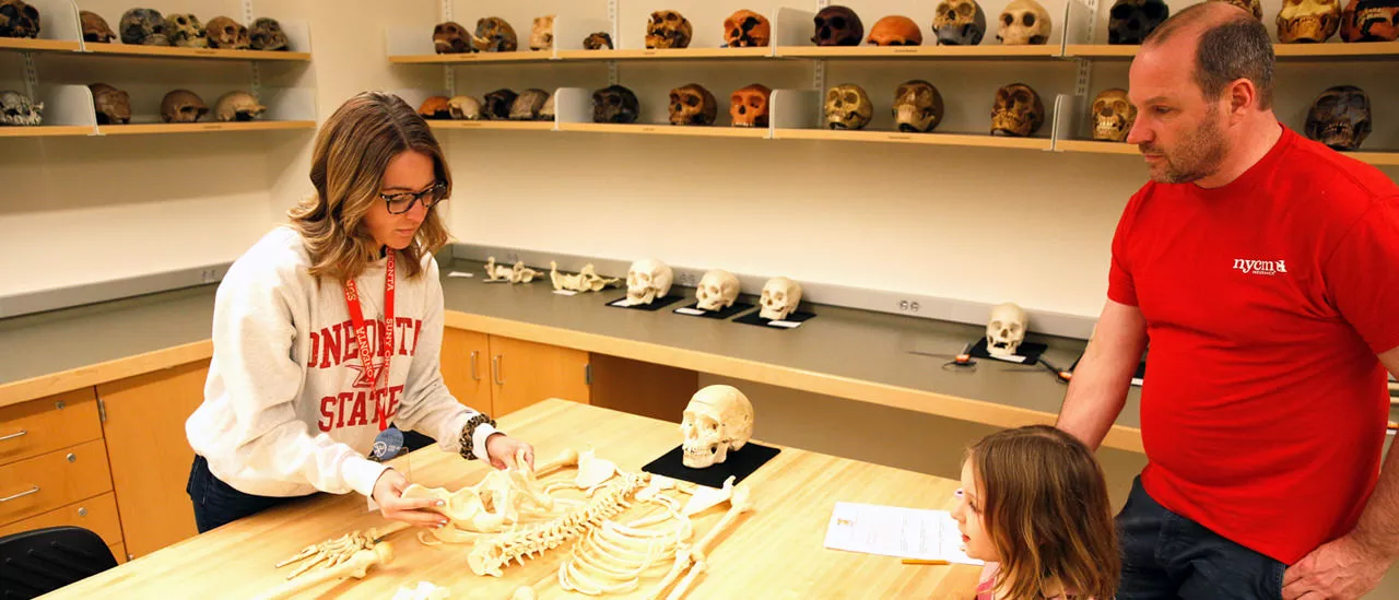 Student presenting a human skeleton to a father and daughter.