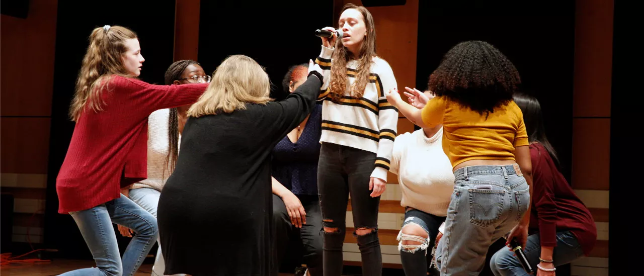 Girl singing with group of students around her.