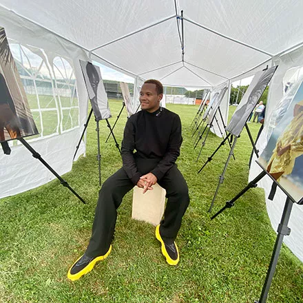 The event’s featured artist, photographer Bertram Knight, a Class of 2019 alumnus, sits inside a tent with his photos on display