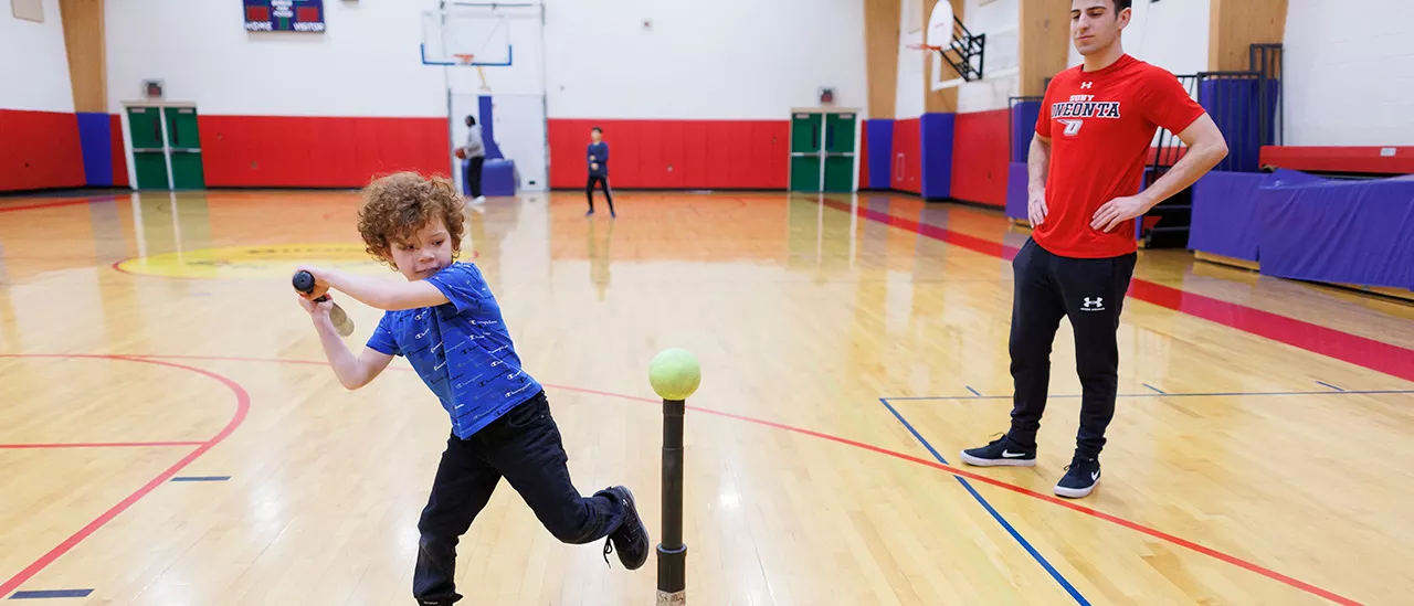 Exercise Science student teaching a child how to play tee ball.