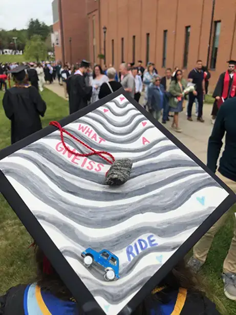 Decorated graduation cap with layers of a rock that says "What a Gneiss Ride," adorned with a rock