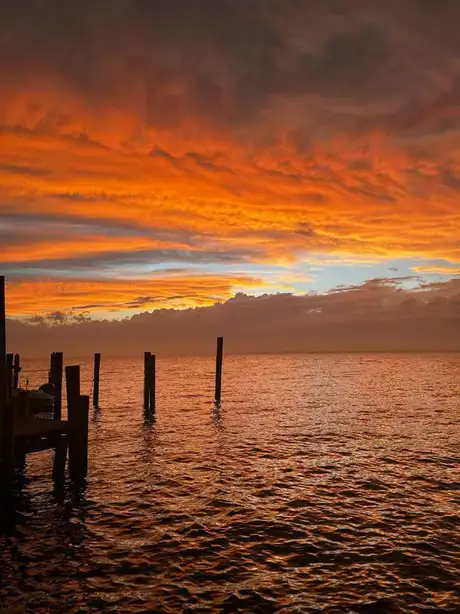 Dramatic sunset over the ocean with vivid orange and red cloud formations, highlighting atmospheric stratification and the interaction of light with layered clouds.