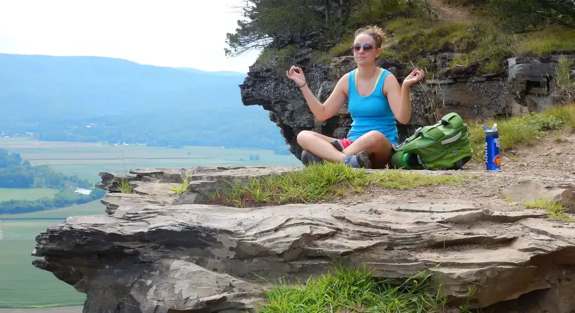 A GEOFYRST student sits cross-legged on a rock outcropping.