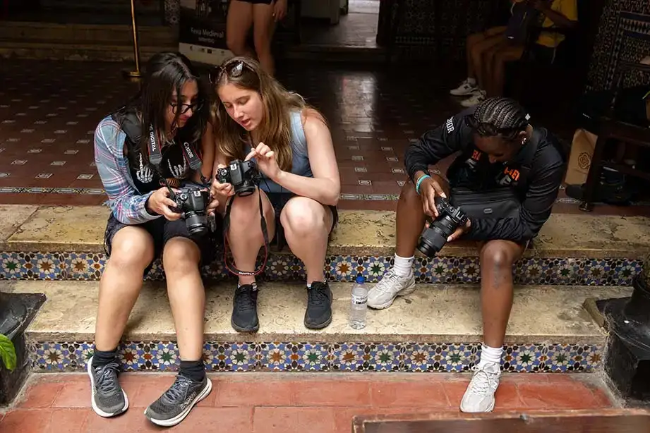 Students sit on steps and compare photos on their digital cameras.