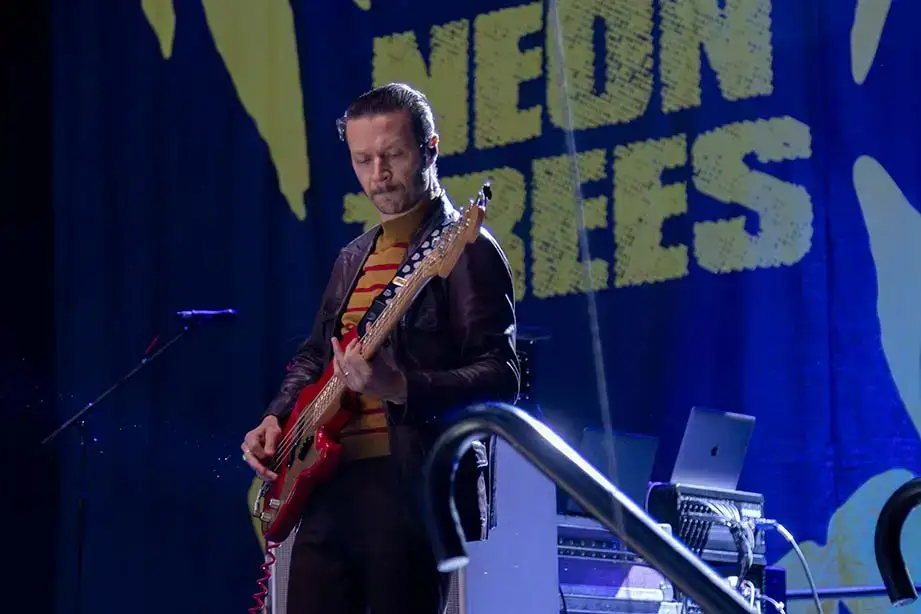 Neon Trees bassist plays on stage in front of a banner featuring the band name.